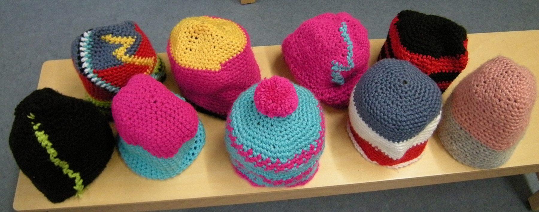 Bunte, handgehäkelte Mützen in verschiedenen Farben und Mustern auf einem Tisch.