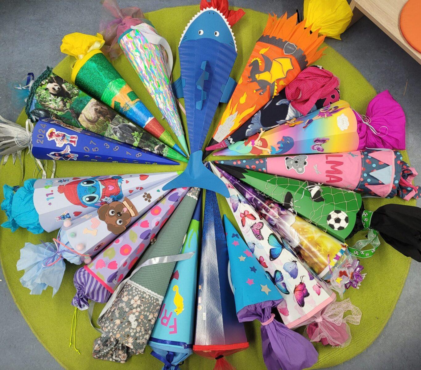 Bunte Schultüten in verschiedenen Designs und Farben, die kreisförmig auf einem grünen Teppich angeordnet sind. Die Schultüten sind kreativ gestaltet und zeigen Motive wie Tiere, Fußball, Regenbogen und mehr, ideal für den Schulanfang.